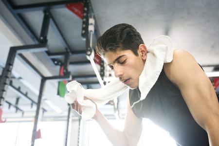 Young fit hispanic man in gym wiping sweat off his faceの写真素材