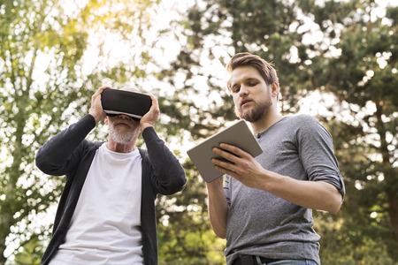 Young man and his senior father with VR glasses outdoors.の写真素材
