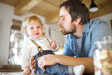 Young father at home with his little son eating biscuit together.の写真素材