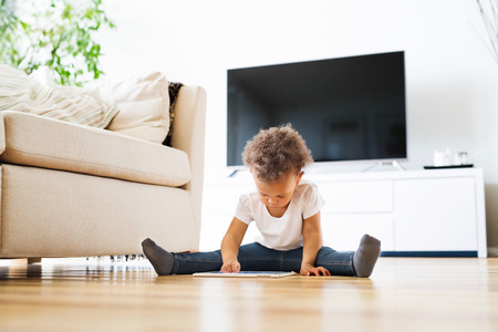 Little mixed-race girl at home playing game on tablet.の写真素材