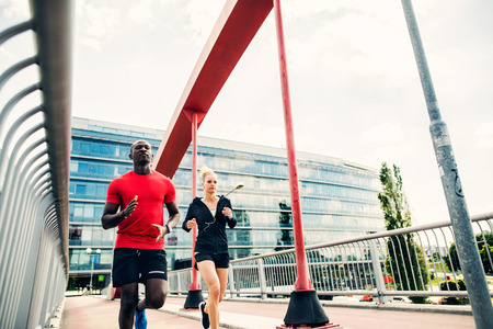 Young couple in the city running on a bridge.