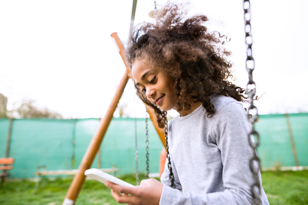 African american girl on swing with smart phone texting.の写真素材