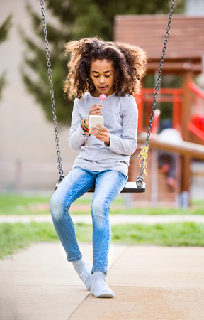 African american girl on swing with smart phone texting.の写真素材