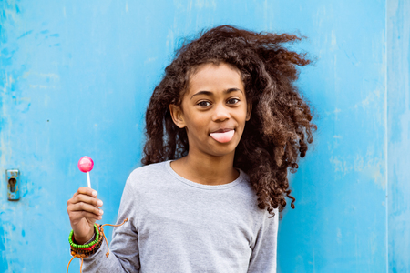African american girl with curly hair outdoors eating lollipop.