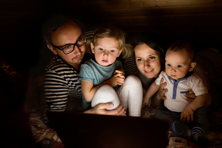 Young parents with little children and laptop at night.の写真素材
