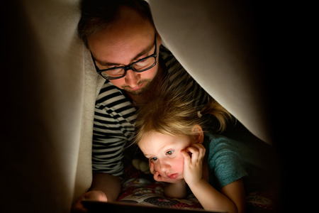 Father with tablet and little daughter at home at night.の写真素材