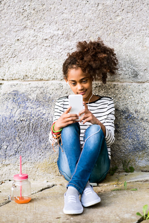 Beautiful african american girl with smart phone and drink.の写真素材
