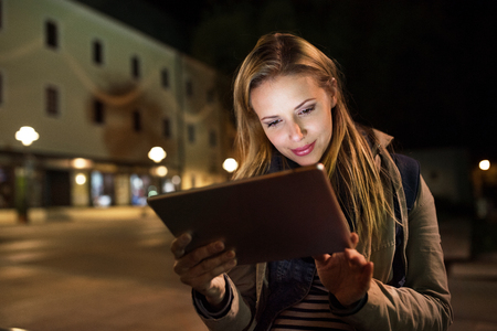 Woman in the city at night holding tablet, reading something.の写真素材
