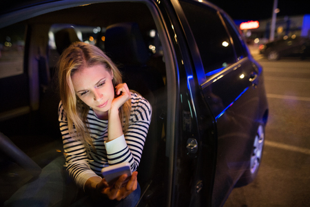 Woman with smartphone in her car at night.の写真素材