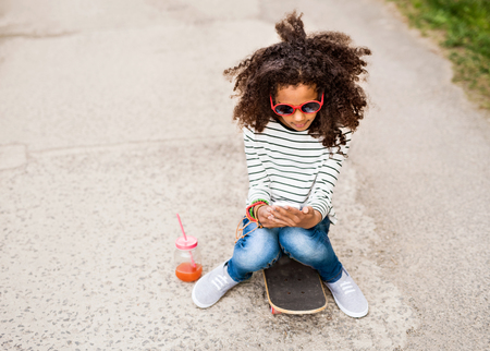Beautiful african american girl with smartphone and skateboard.の写真素材