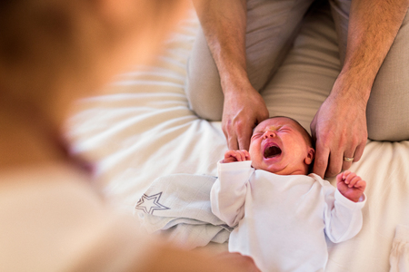Unrecognizable parents at home dressing their baby girl on bed.の写真素材