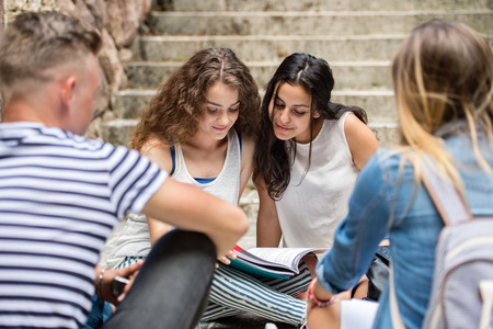 Teenage students sitting on stone steps in front of university.の写真素材