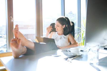 Businesswoman in her office sitting with legs on desk.の写真素材