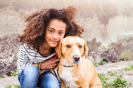 African american girl with her dog against concrete wall.