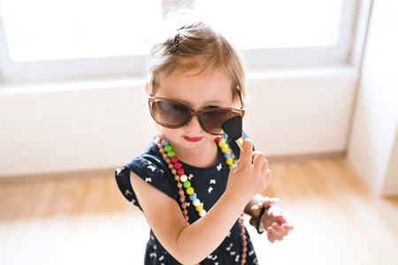 Cute little girl in dress and big sunglasses at home.の写真素材