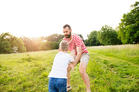 Hipster father and little son on green meadow. Sunny summer day.の写真素材
