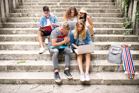 Teenage students with laptop outside on stone steps.の写真素材