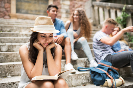 Teenage student girl sitting on stone steps reading a book.の写真素材