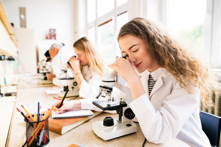 Beautiful high school students with microscopes in laboratory.の写真素材