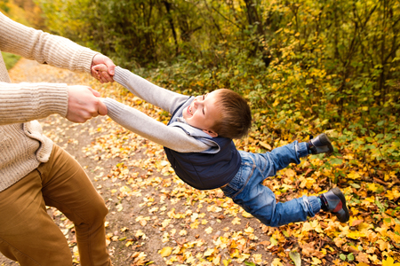 Unrecognizable father with son, spinning him. Autumn nature.の写真素材