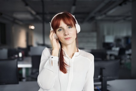 Businesswoman with big earphones in her office.の写真素材