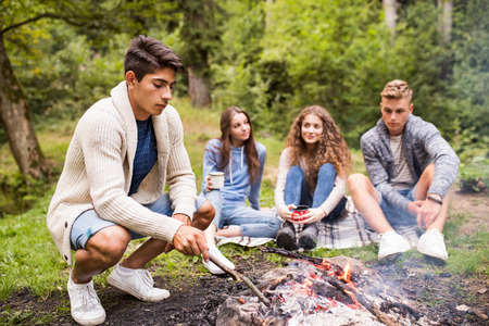 Teenagers camping in nature, sitting at bonfire.の写真素材