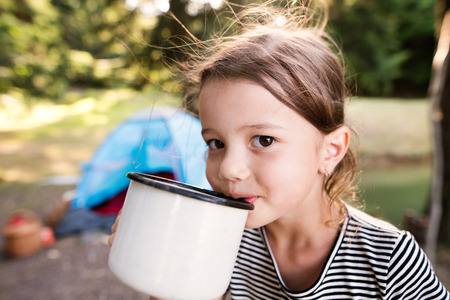 Cute little girl camping outdoors, drinking water.の写真素材