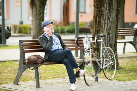 Senior man with bicycle and smart phone, making phone callの写真素材