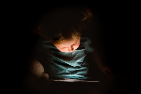 Little girl at home at night watching something on tablet.の写真素材