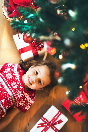 Little girl lying under Christmas tree among presents,の写真素材