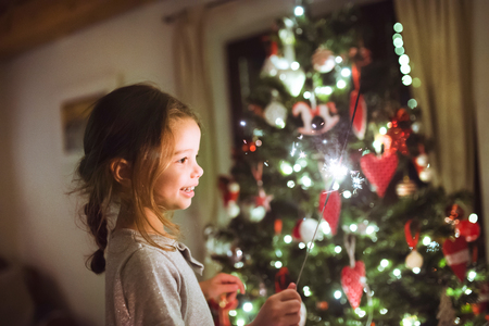 Little girl with a sparkler in front of Christmas tree.の写真素材