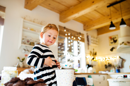 Cute little girl in striped dress sitting on kitchen table.の写真素材