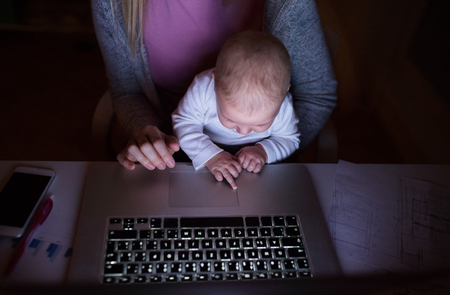 Unrecognizable mother with son on lap, working on laptopの写真素材