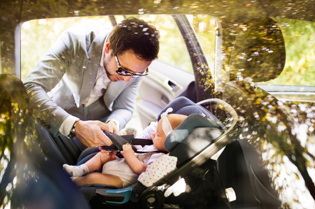 Young father putting baby girl in the car.