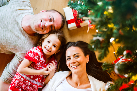 Young family lying under Christmas tree among presents,の写真素材