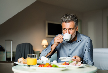 Mature businessman having breakfast in a hotel room.の写真素材