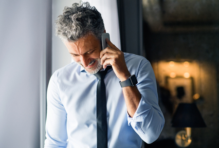 Mature businessman with smartphone in a hotel room.の写真素材