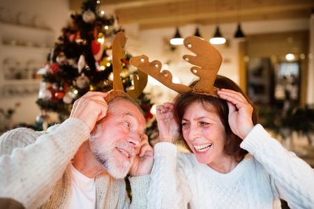 Senior couple in front of Christmas tree wearing deer antlers.の写真素材