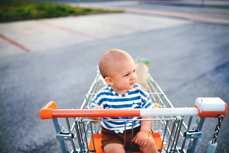 Baby boy sitting in the shopping trolley outside.の写真素材