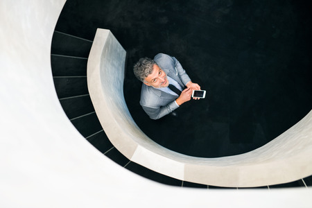 Businessman with smartphone standing at staircase.の写真素材
