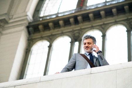 Mature businessman with smartphone on a train station.の写真素材