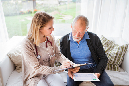 Health visitor and a senior man with tablet during home visit.の写真素材