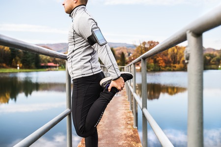 Young athlete with smartphone stretching in park.