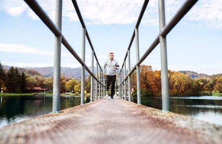 Young athlete with smartphone running in park in autumn.の写真素材