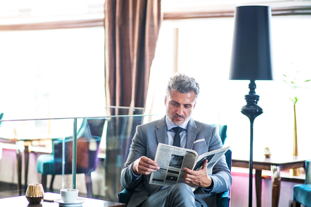 Mature businessman reading newspapers in a hotel lounge.の写真素材