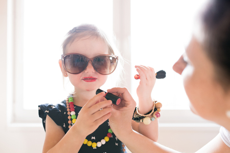 Mother painting lips of her cute little daughter with lipstick.の写真素材