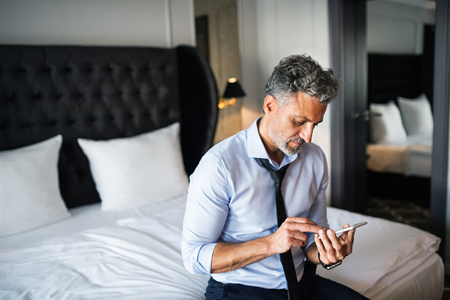 Mature businessman with smartphone in a hotel room.の写真素材
