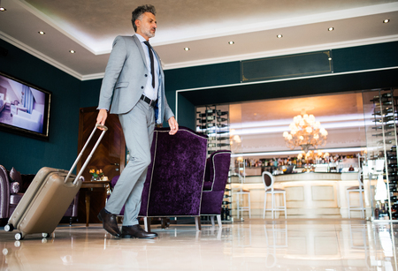 Mature businessman entering hotel with luggage.の写真素材