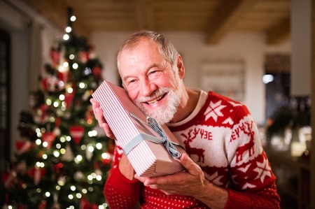 Senior man in front of Christmas tree holding a gift.の写真素材