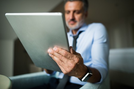Mature, handsome businessman working on a tablet in a hotel room.の写真素材